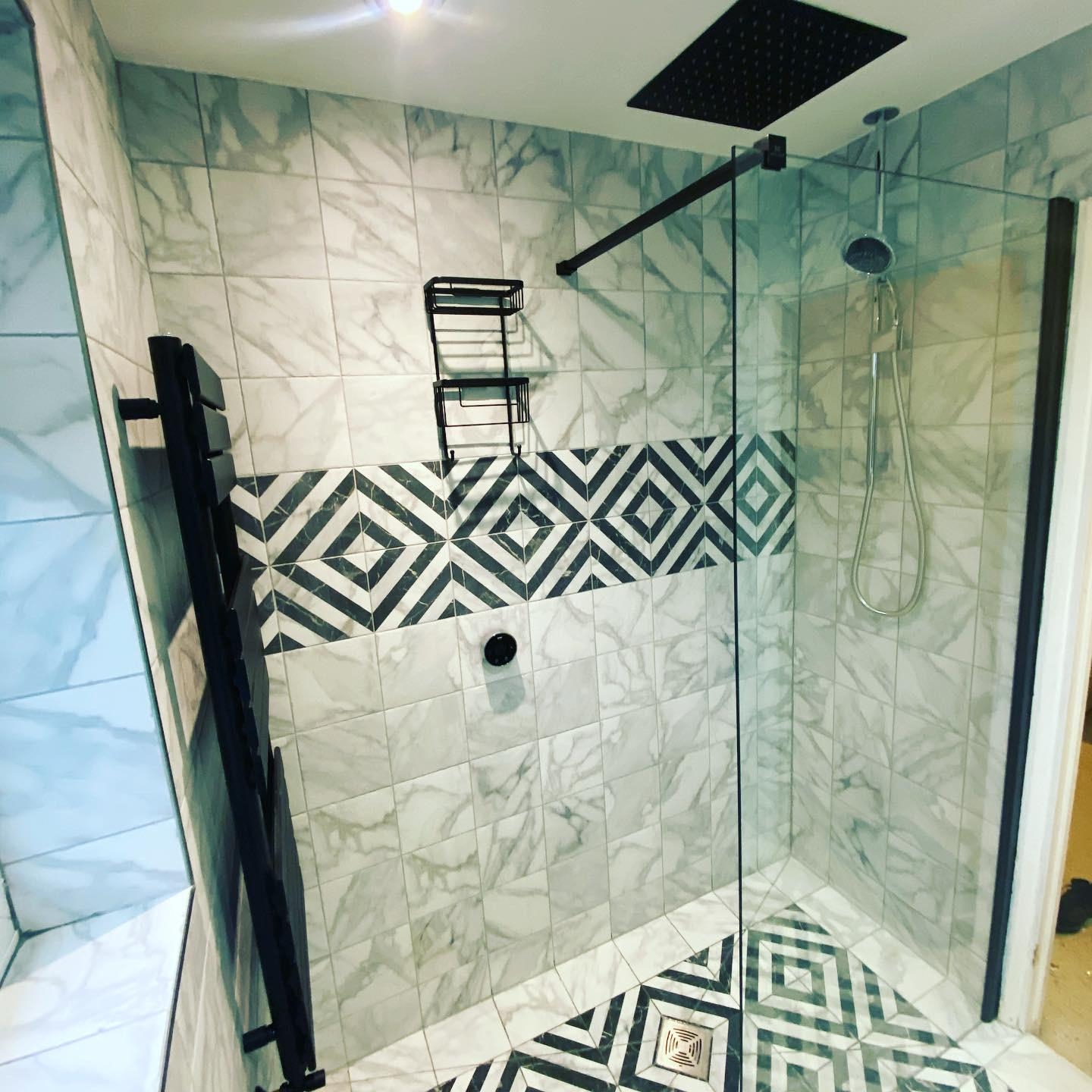 A walk-in shower with a black frame, rainfall head and a black and white diamond tile band