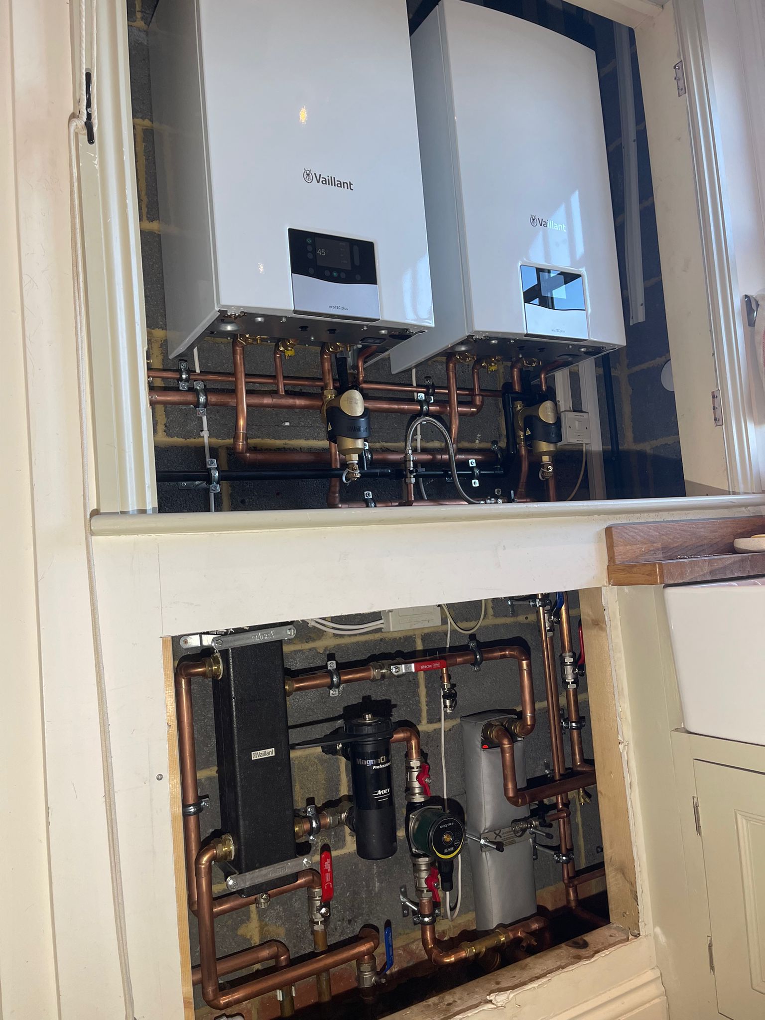 Two Vaillant boilers side by side with copper pipework and controls in the cupboard below