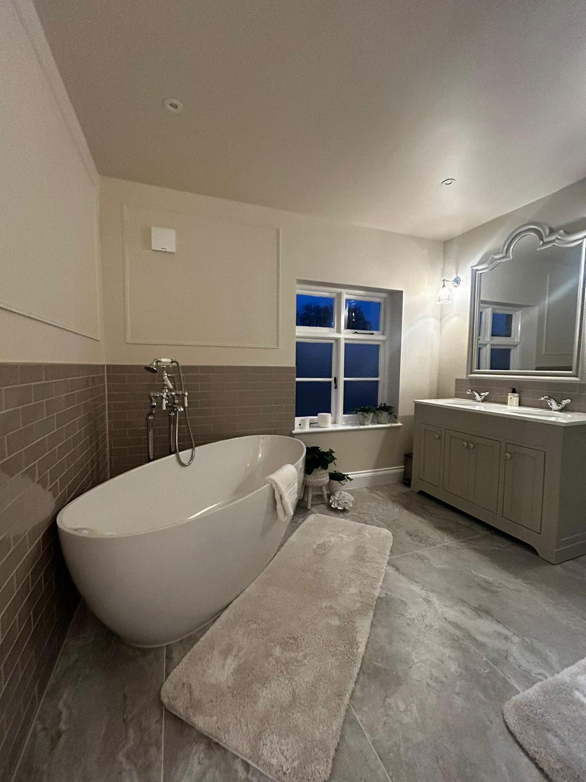 A bathroom with a freestanding bath, a double vanity unit and an arched mirror