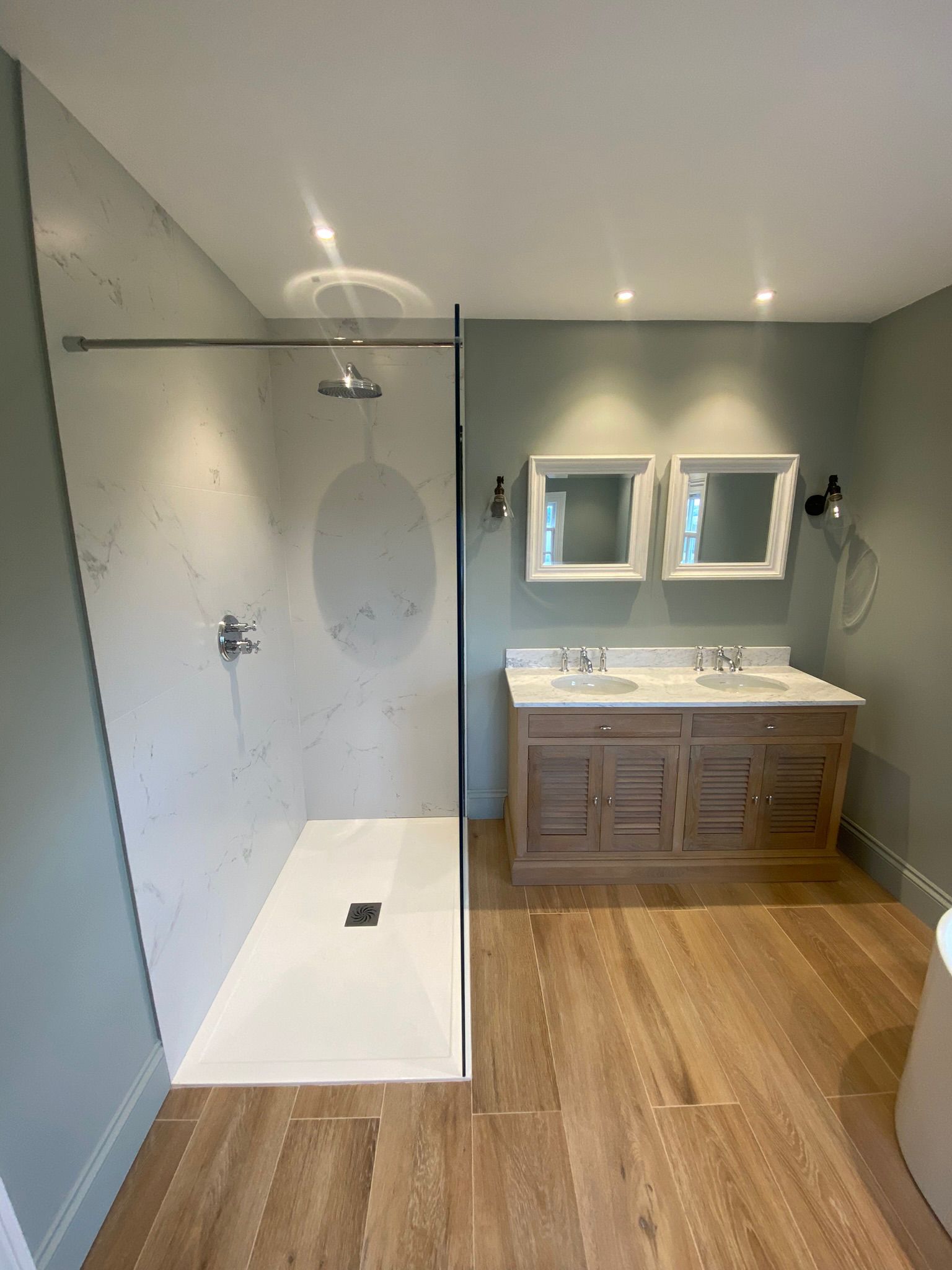 Walk-in shower with a glass panel beside a double vanity on a wood-effect floor